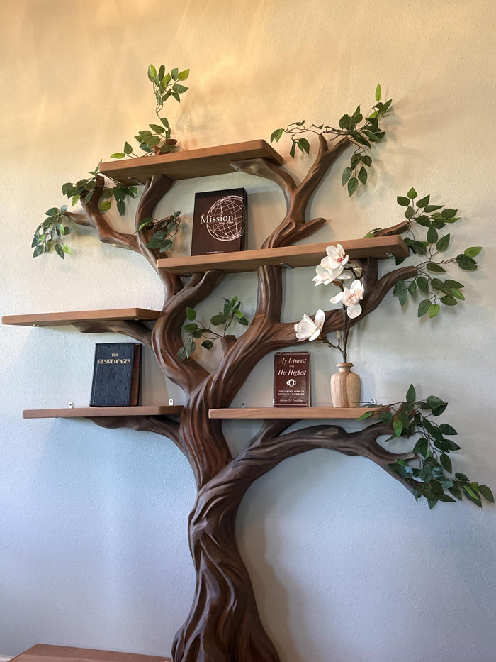 Wooden tree-shaped bookshelf with shelves, books, and decorative items against a light wall.